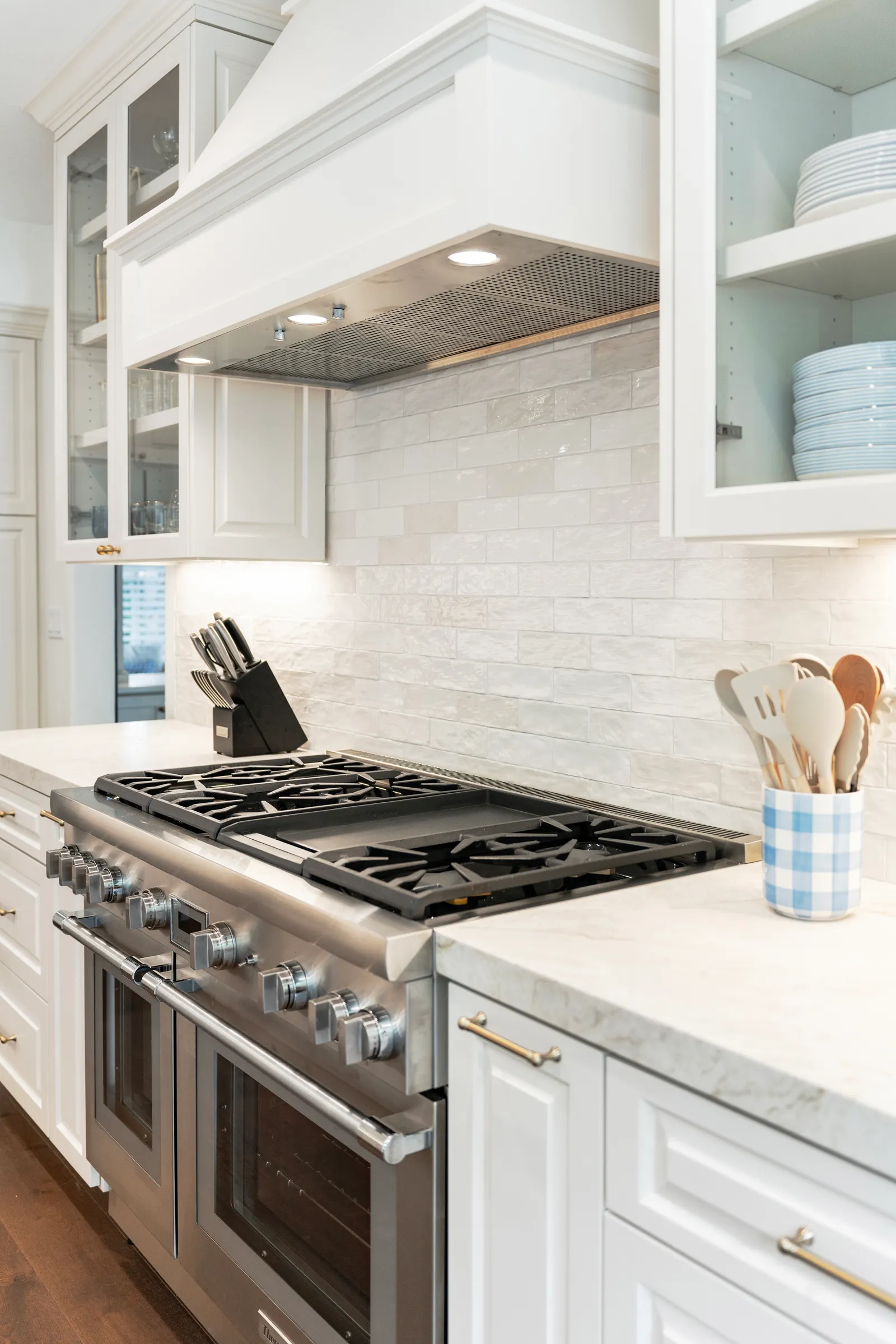 Professional stainless range with a griddle beneath a white custom hood and glossy handmade subway tile backsplash.