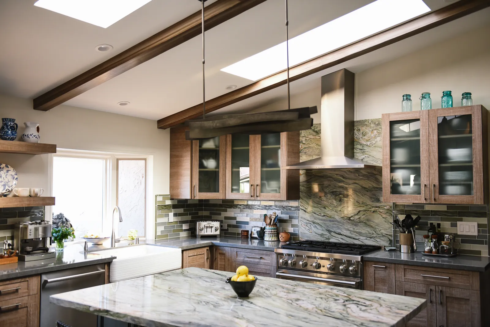 A kitchen with dramatic quartzite backsplash panels, wood cabinets, skylights, exposed beams, and a stainless range.