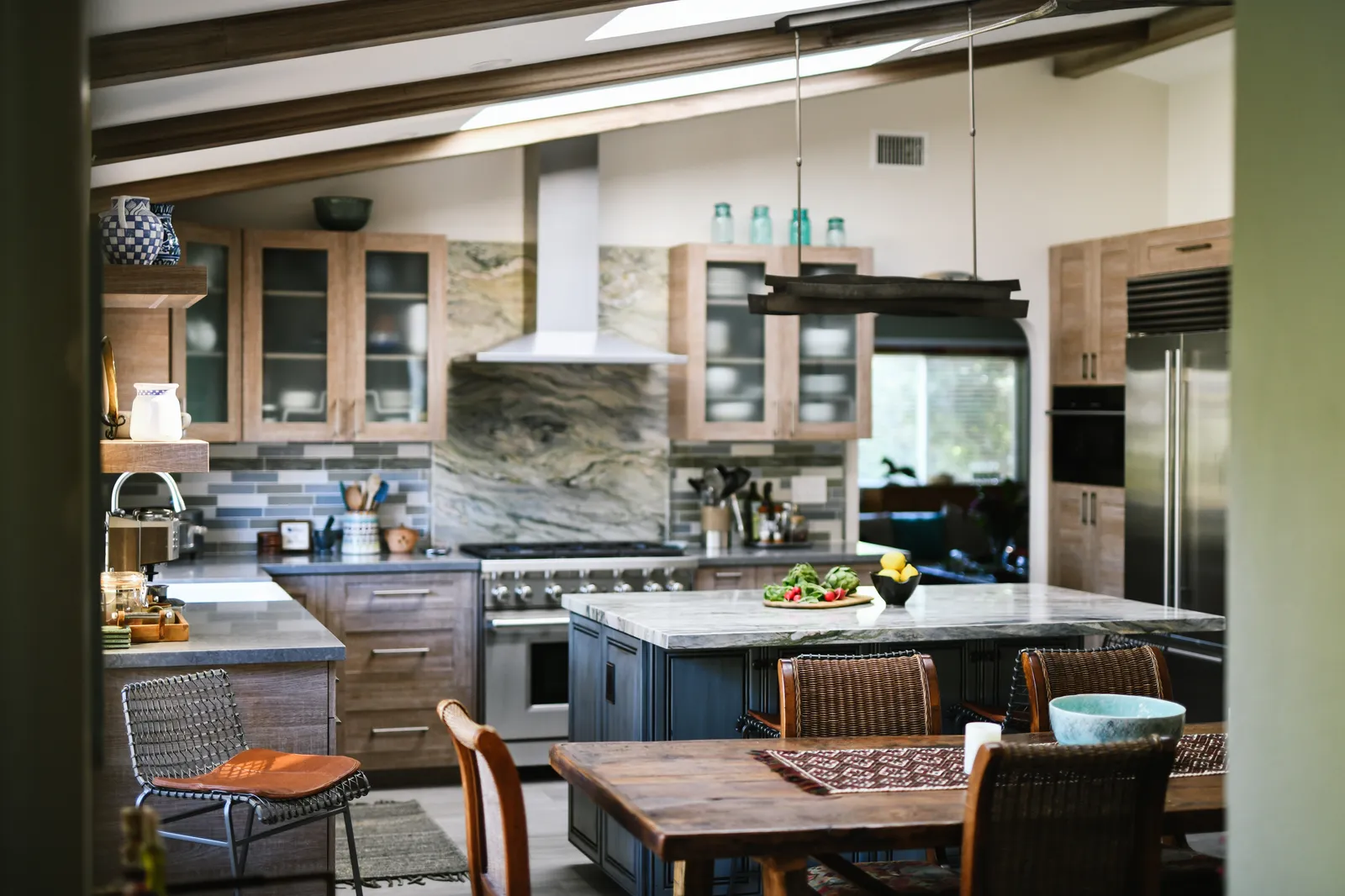 Kitchen with wood-grain cabinetry, dramatic marble backsplash, gray island and exposed ceiling beams.