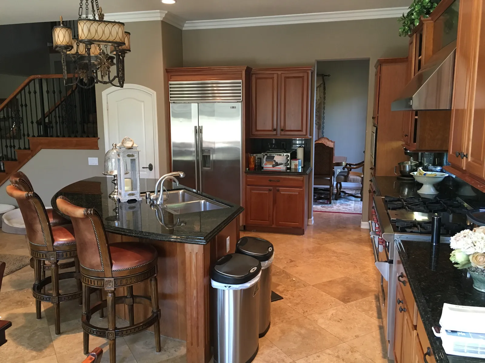 A traditional kitchen with cherry cabinets, black granite counters, a stainless refrigerator, and leather barstools at an island.