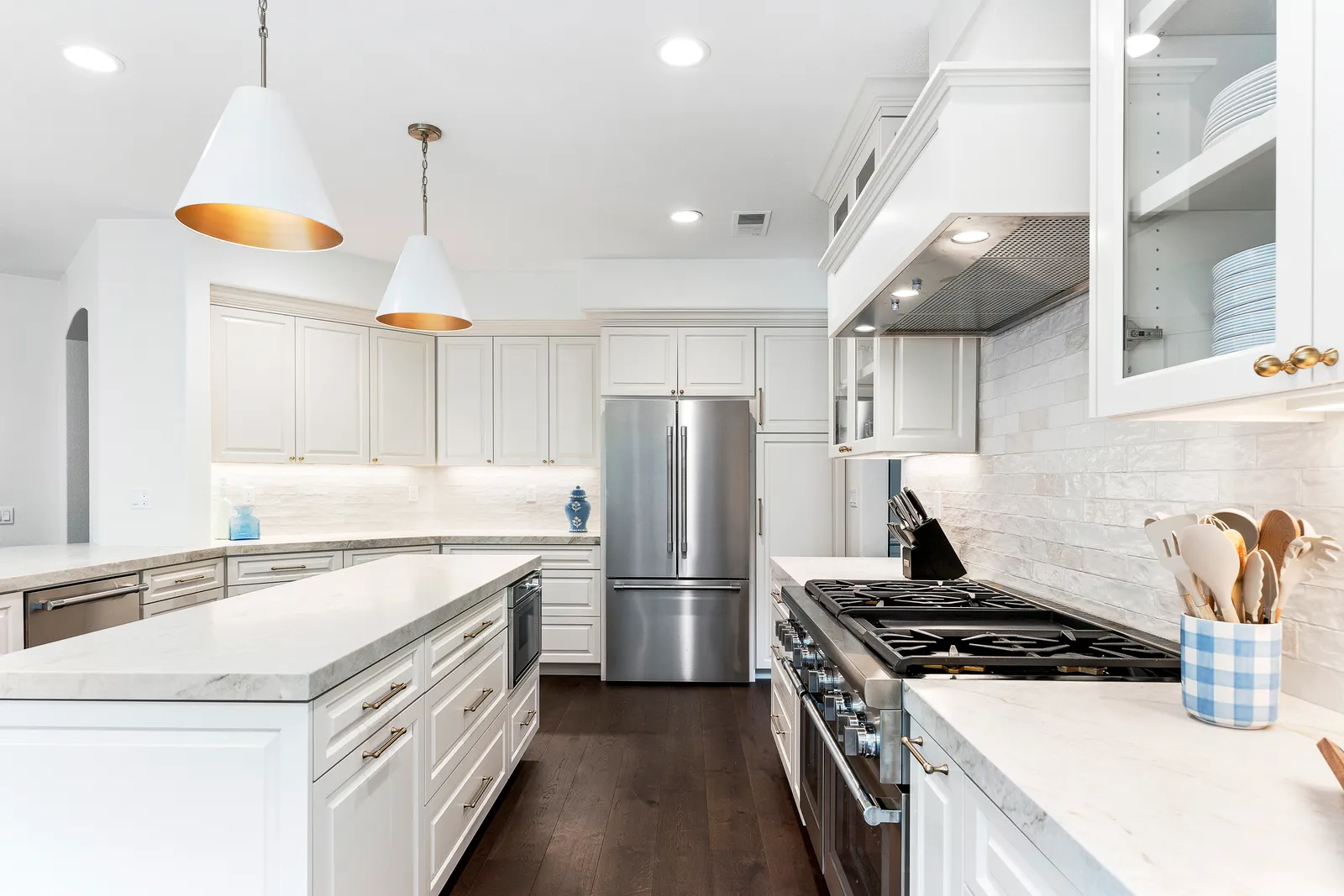 White kitchen with cone pendants over a marble island, pro-style range, and brick-look backsplash.