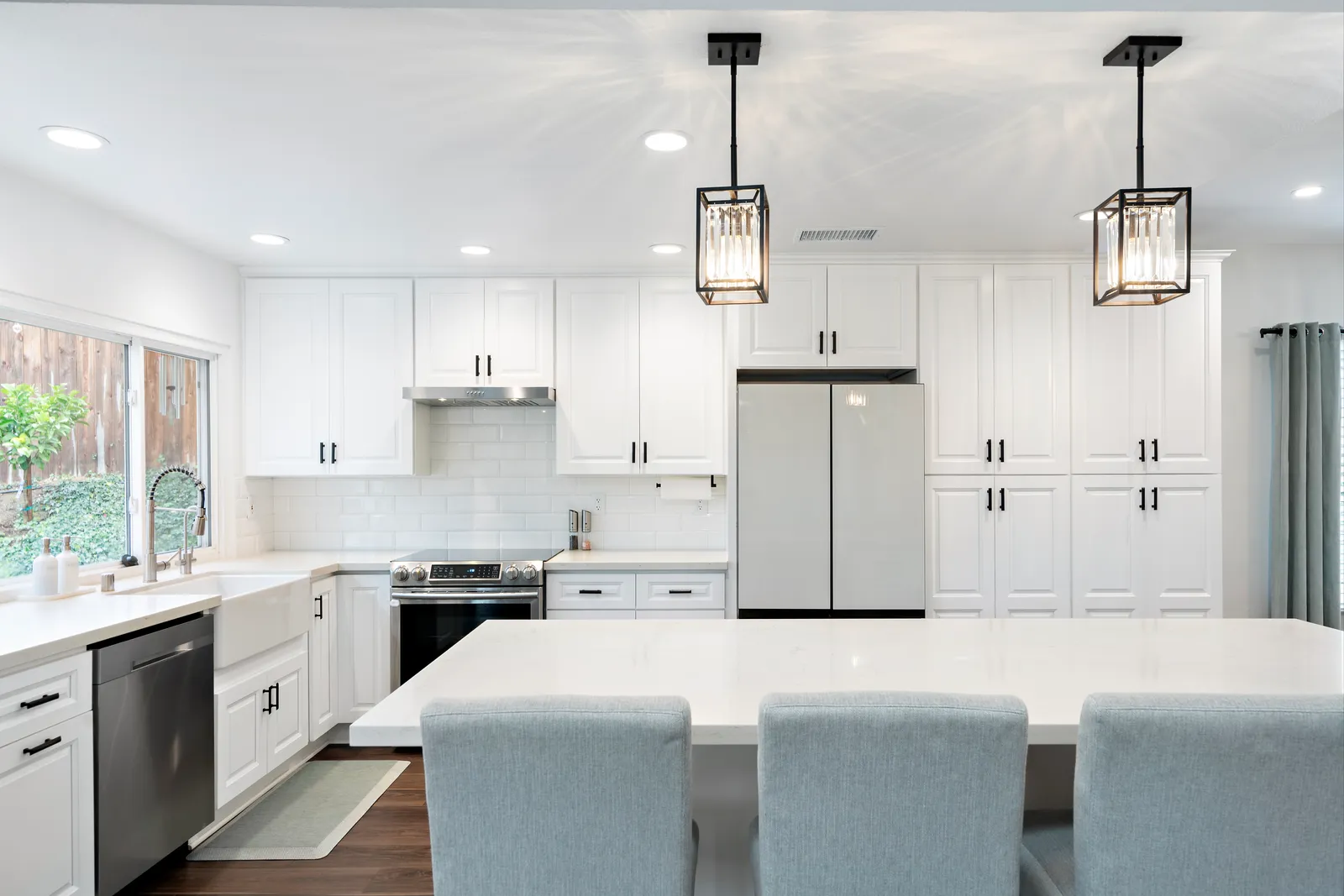 White kitchen with subway tile, farmhouse sink, caged crystal pendants and pale blue counter chairs.