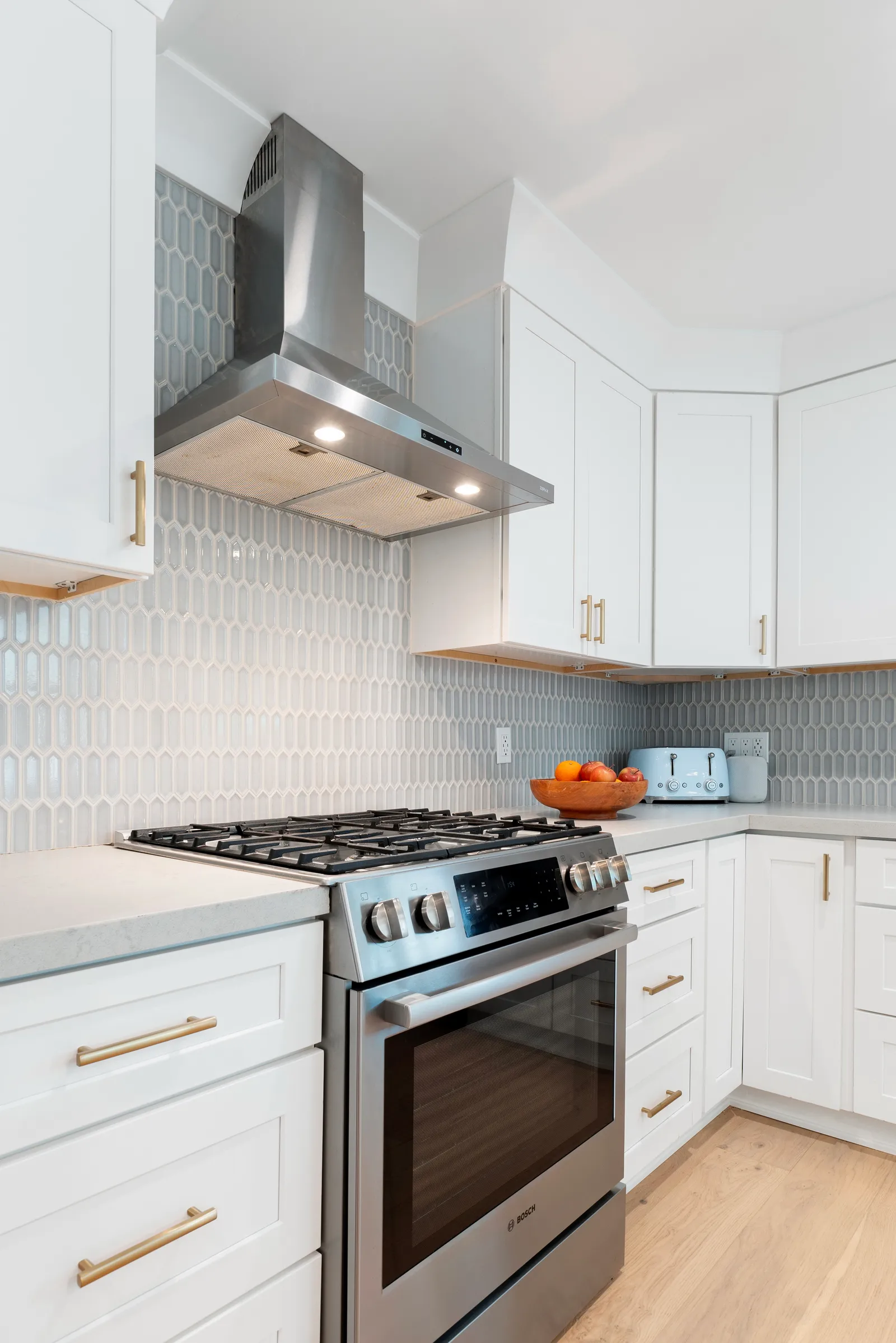 White kitchen with picket-shaped tile backsplash, brass hardware and stainless slide-in range.