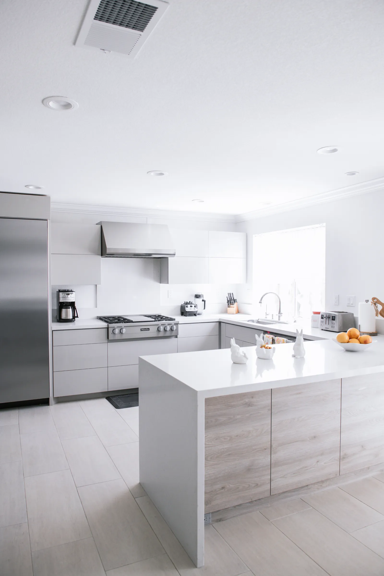 A bright modern kitchen with white flat-panel cabinets, a waterfall-edge peninsula, and stainless steel appliances.