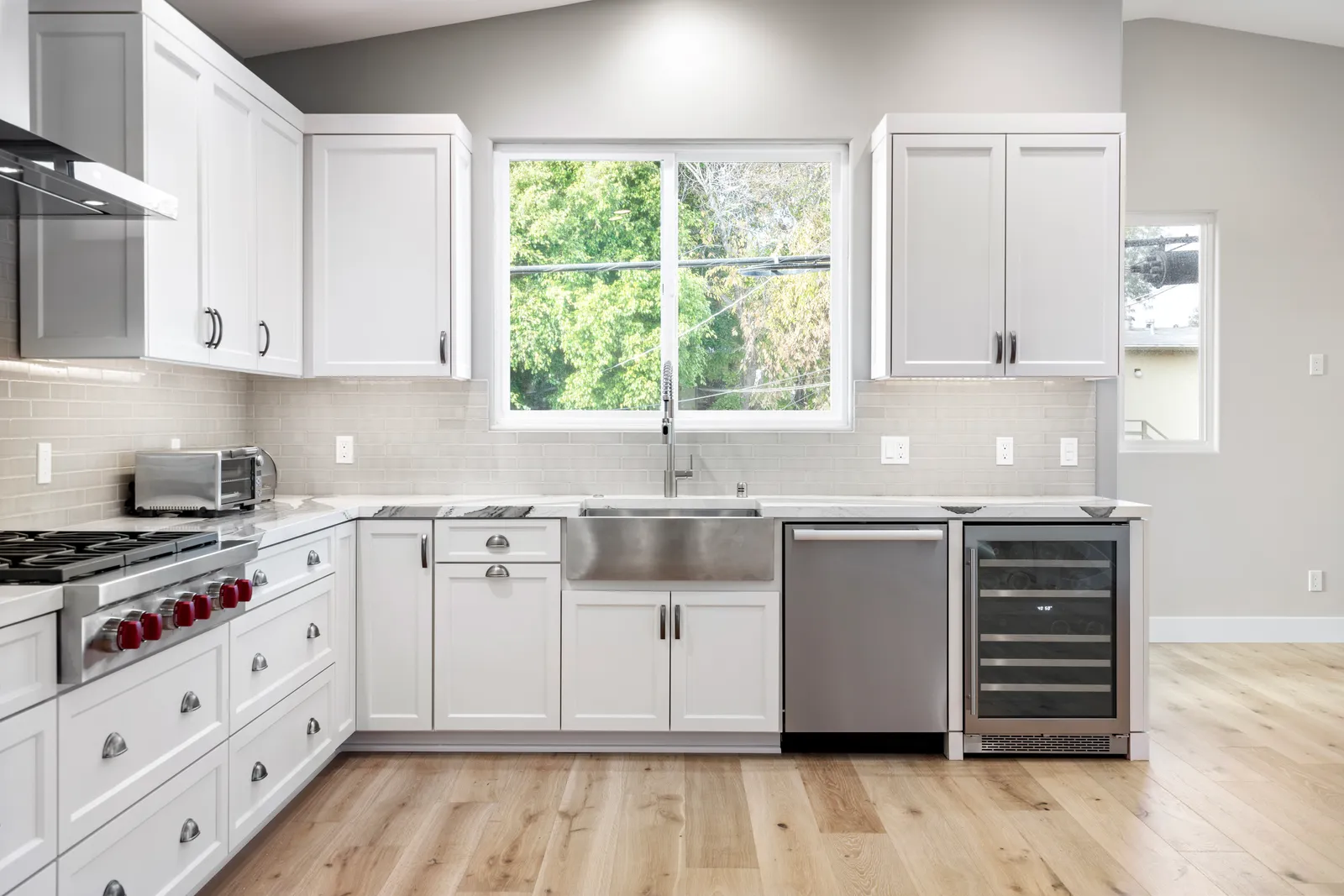 A white shaker kitchen with a professional gas rangetop, farmhouse sink, marble-look counters, and light oak flooring.