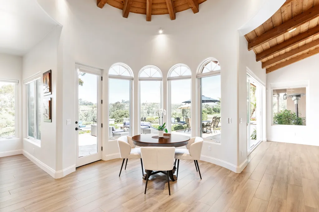 A bright breakfast nook with a round wood table, cream chairs, arched windows, and a wood-beamed ceiling.