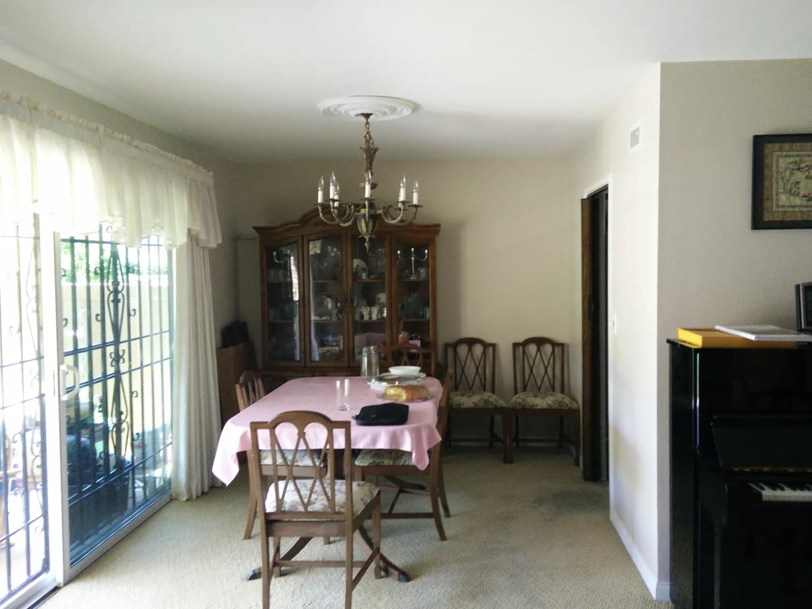 A dining room with a wood dining set, china cabinet, chandelier, and sliding glass door.