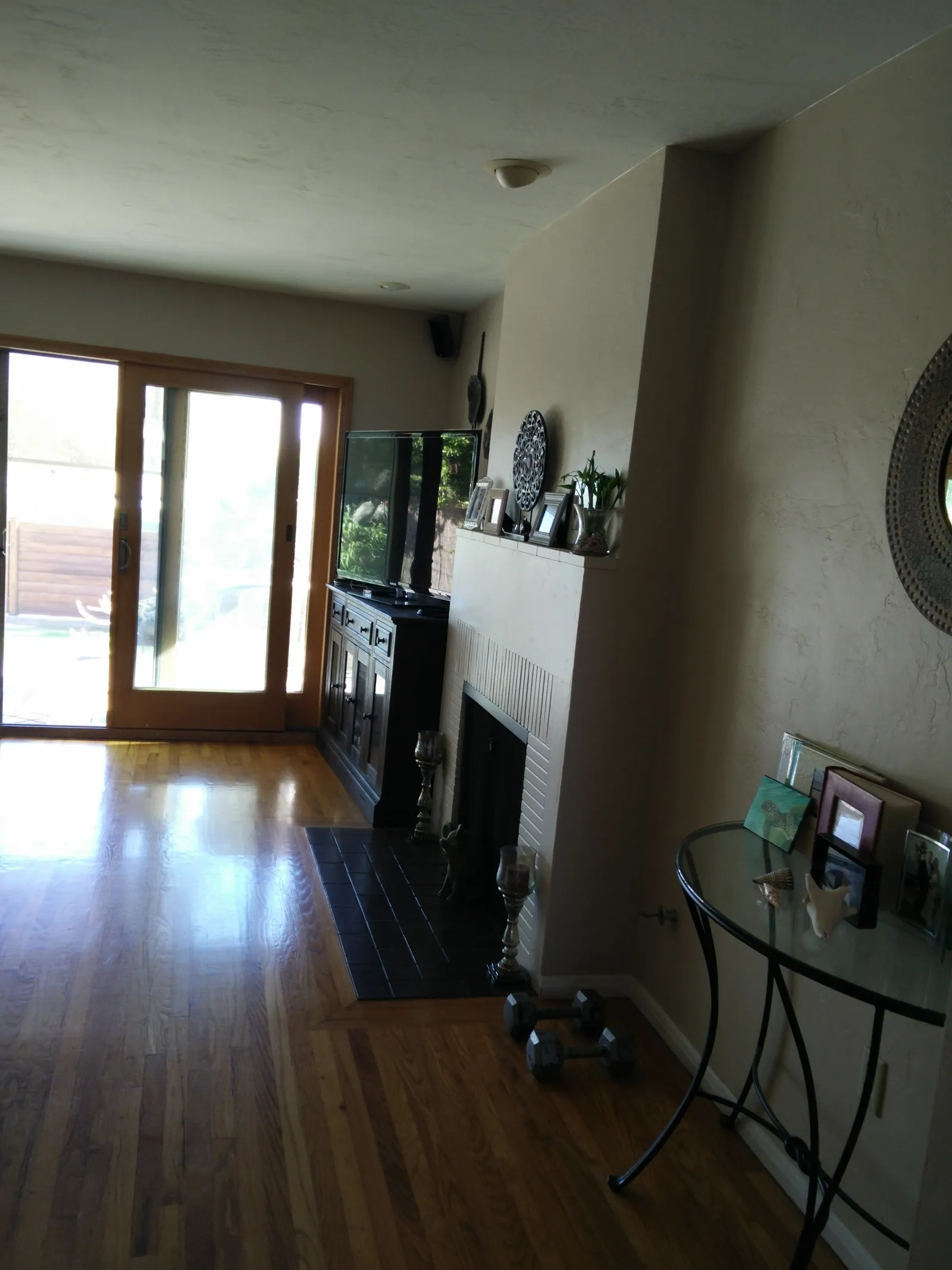 A dated living room with a painted brick fireplace, wood sliding patio doors, and glossy oak floors.