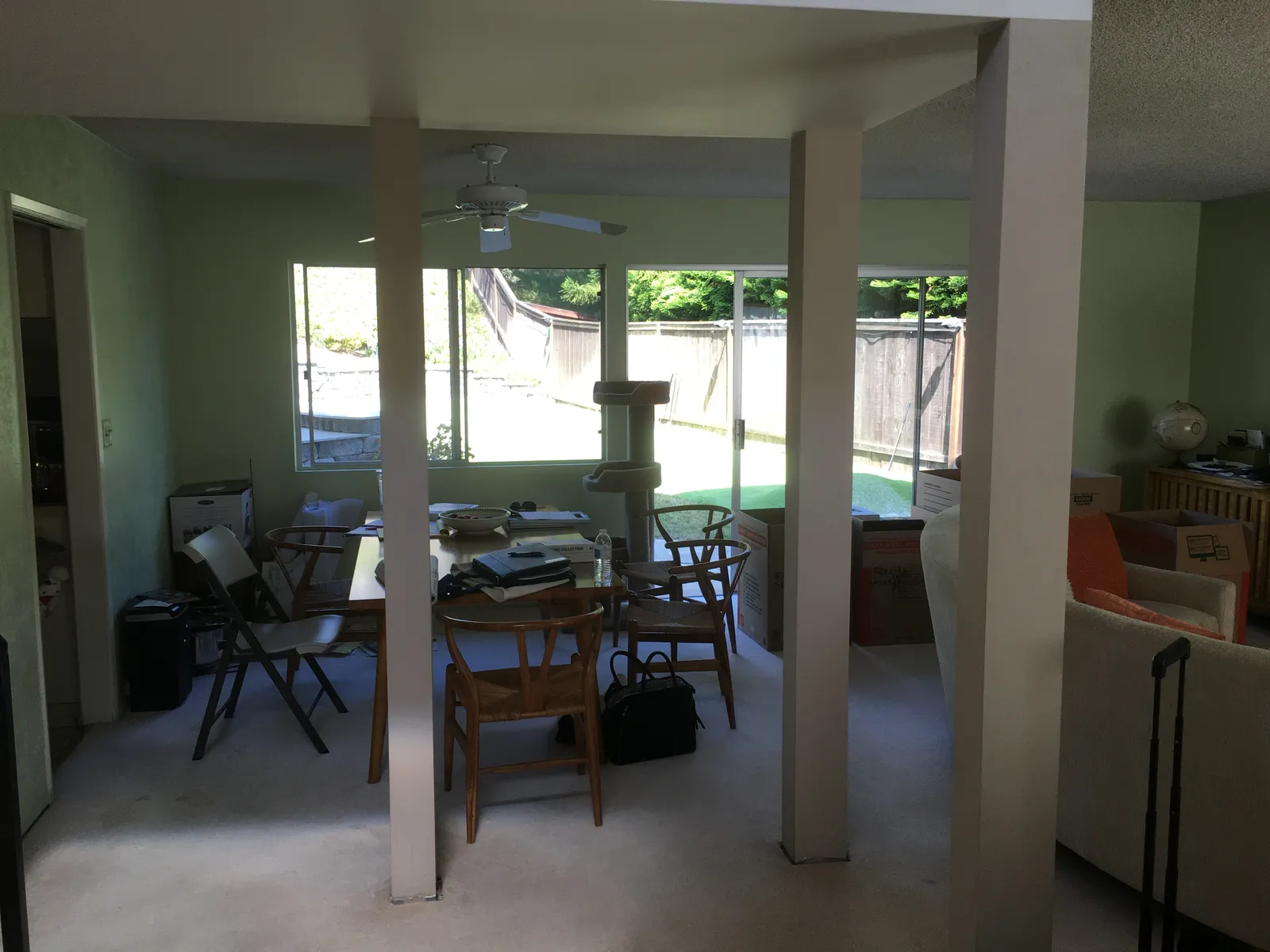 A dining area with a wood table and wishbone chairs surrounded by moving boxes, seen between structural posts.