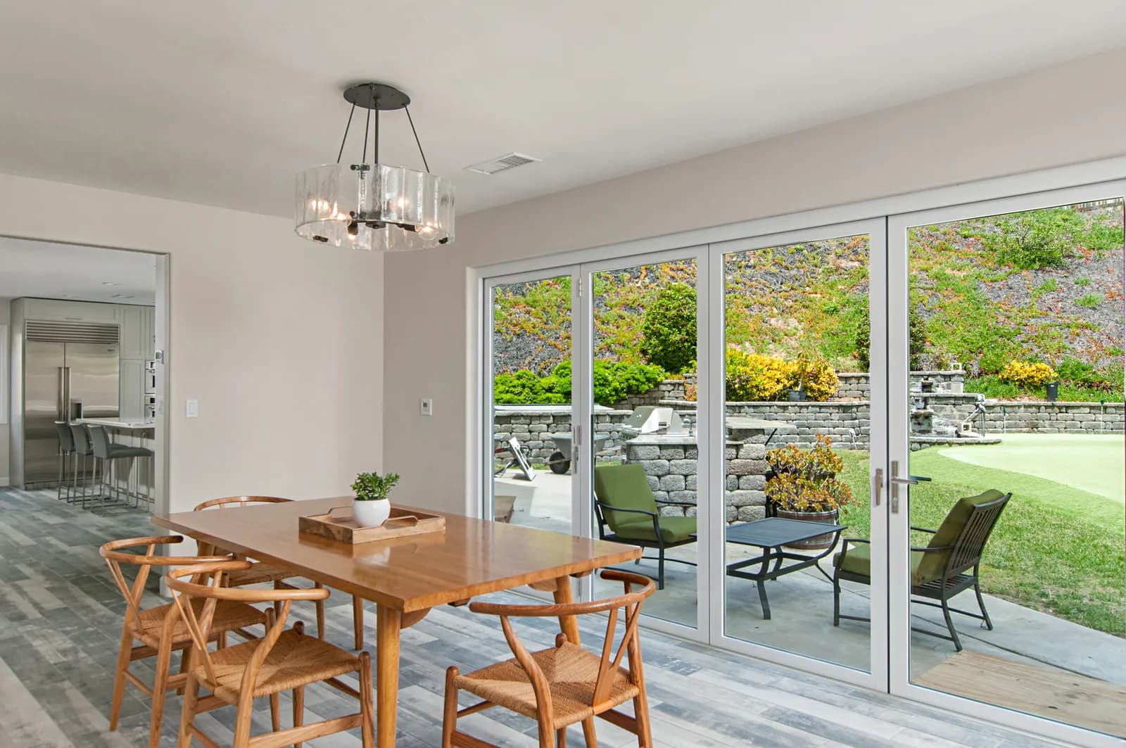 A dining area with a wood table, wishbone chairs, and folding glass doors opening to a terraced backyard patio.