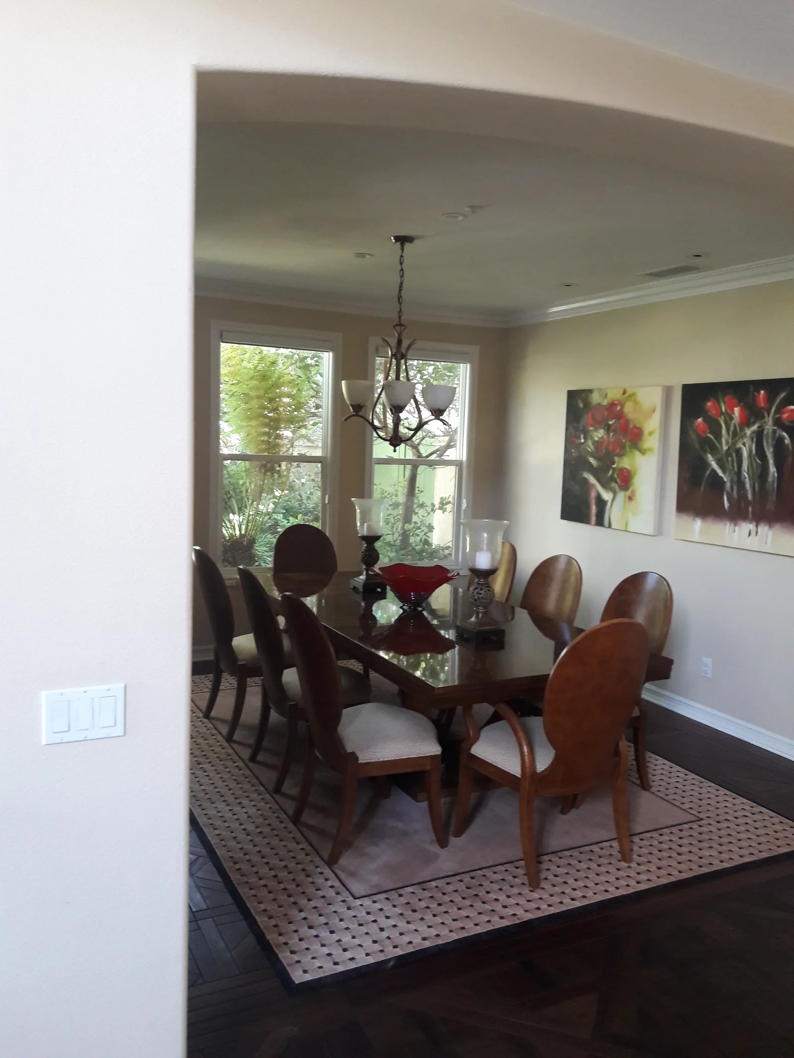 A formal dining room with a long polished table, oval-back chairs, and a small chandelier.