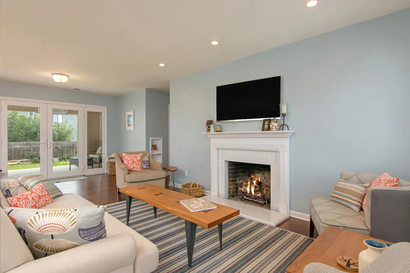 Coastal living room with light blue walls, a white fireplace with a lit fire, and a mounted television.