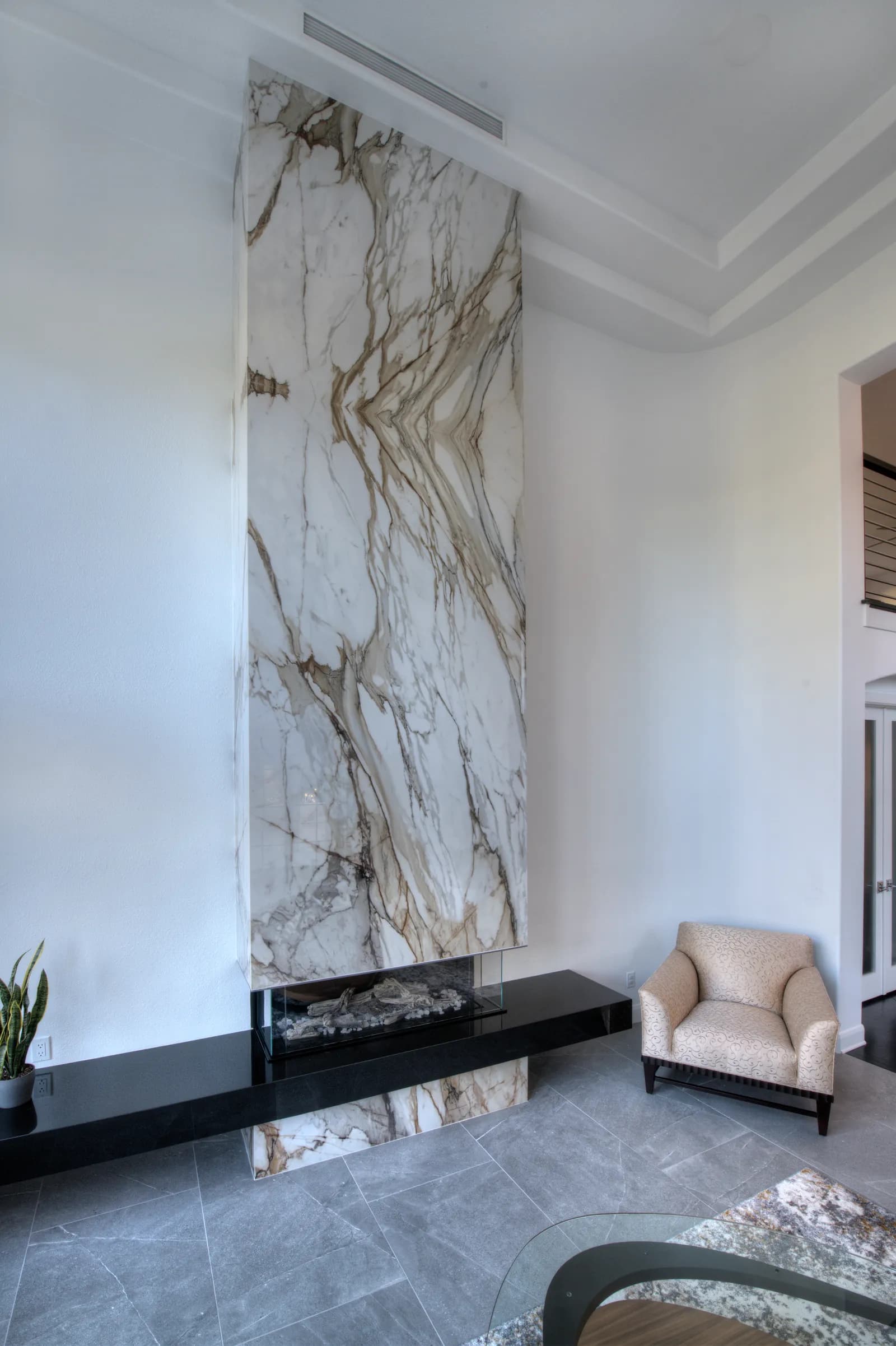 Floor-to-ceiling book-matched marble fireplace surround with a black stone hearth bench and an armchair beside it.