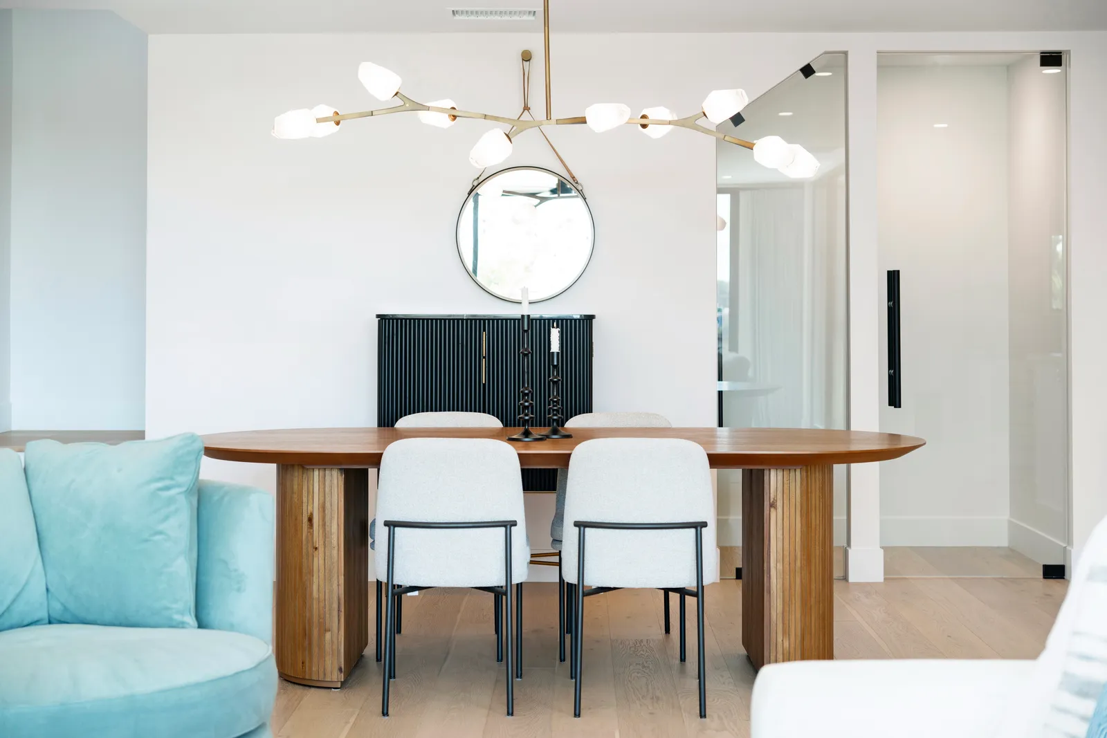 A dining room with an oval wood table, upholstered chairs, and a branching brass chandelier.