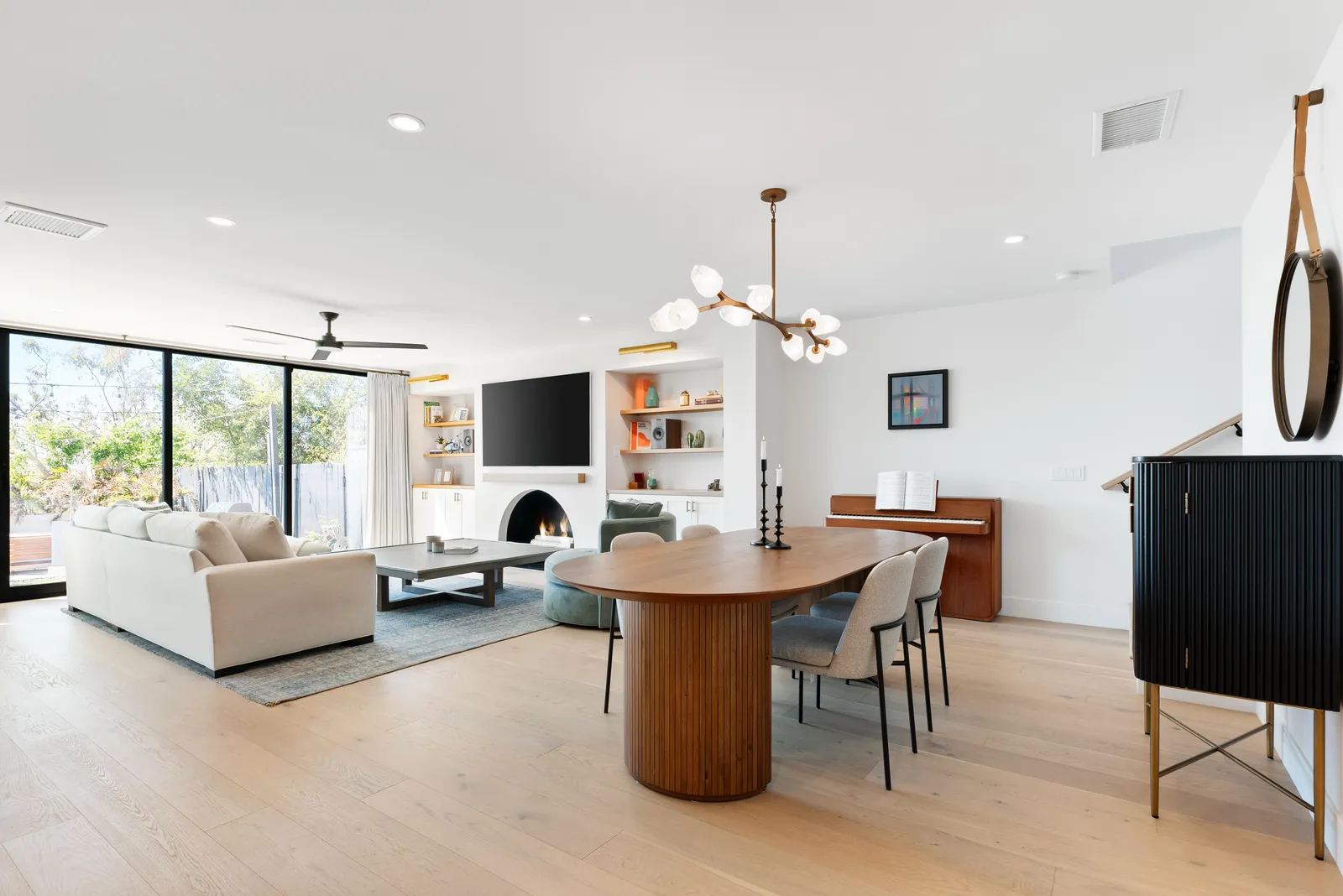 Open living and dining room with an oval wood table, upright piano, and arched fireplace.