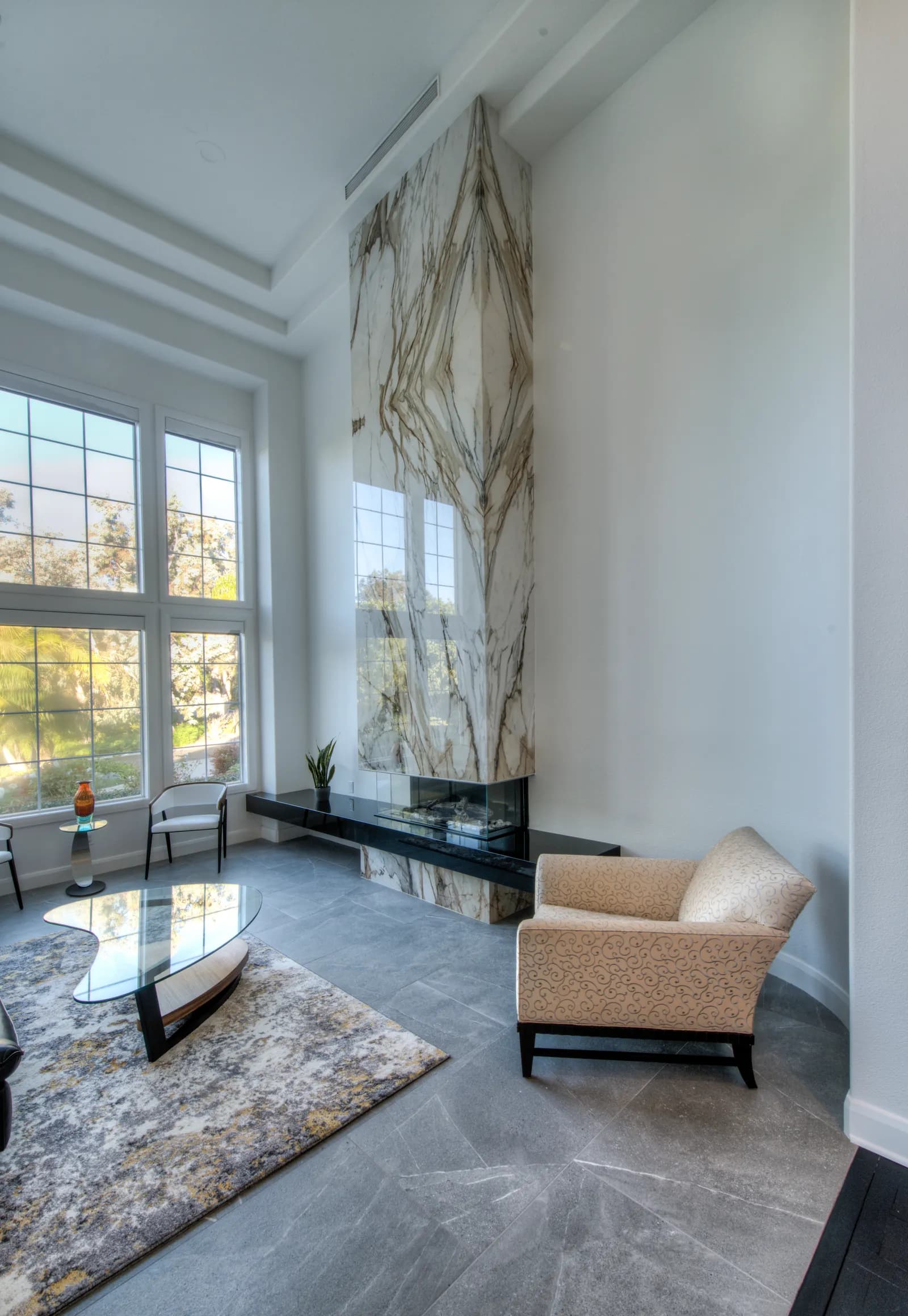 Formal living room with a dramatic two-story bookmatched marble fireplace, floating black hearth, and tall grid windows.