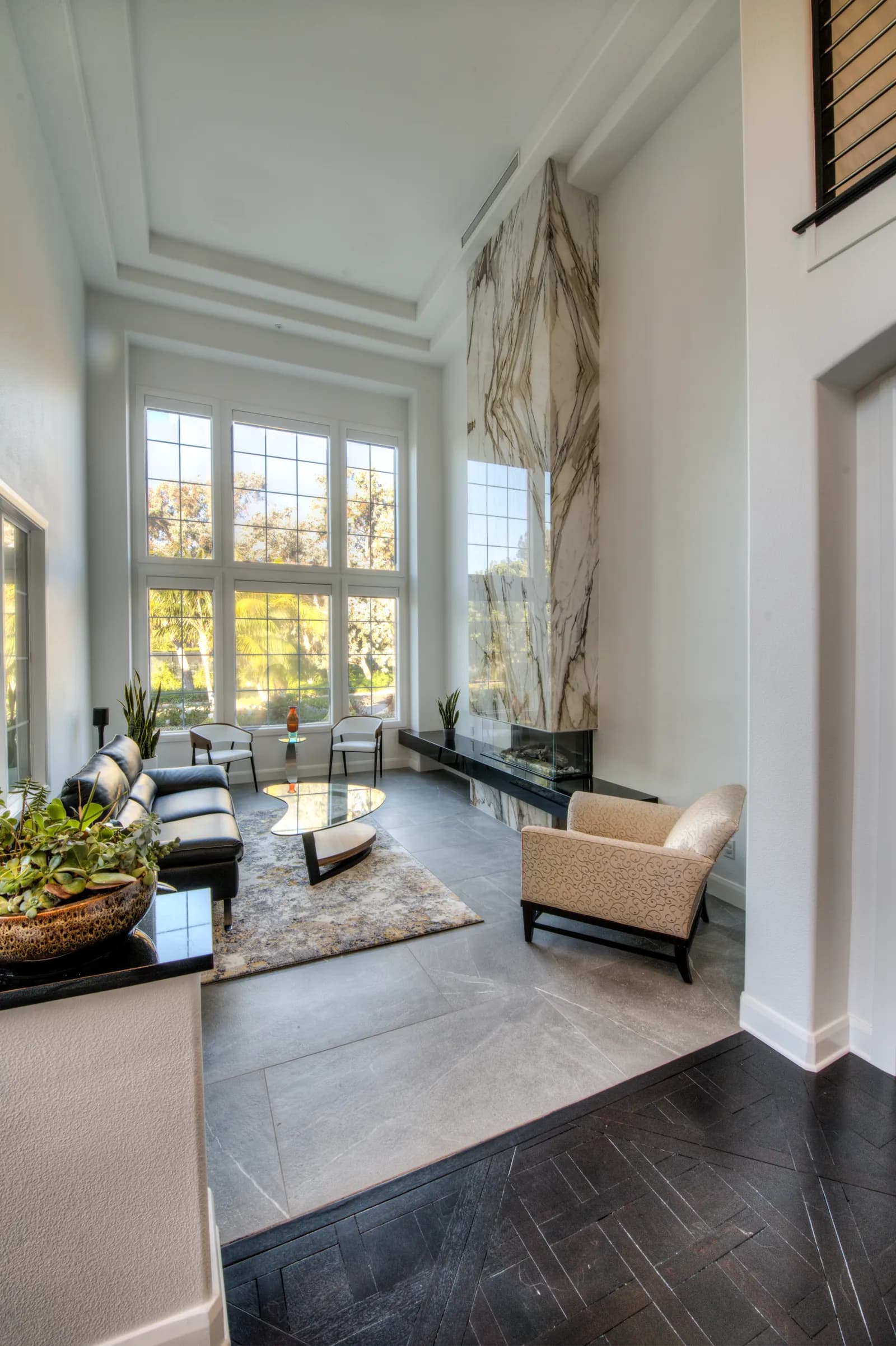 Double-height sitting room with a floor-to-ceiling marble fireplace, tall grid windows, and modern furniture.