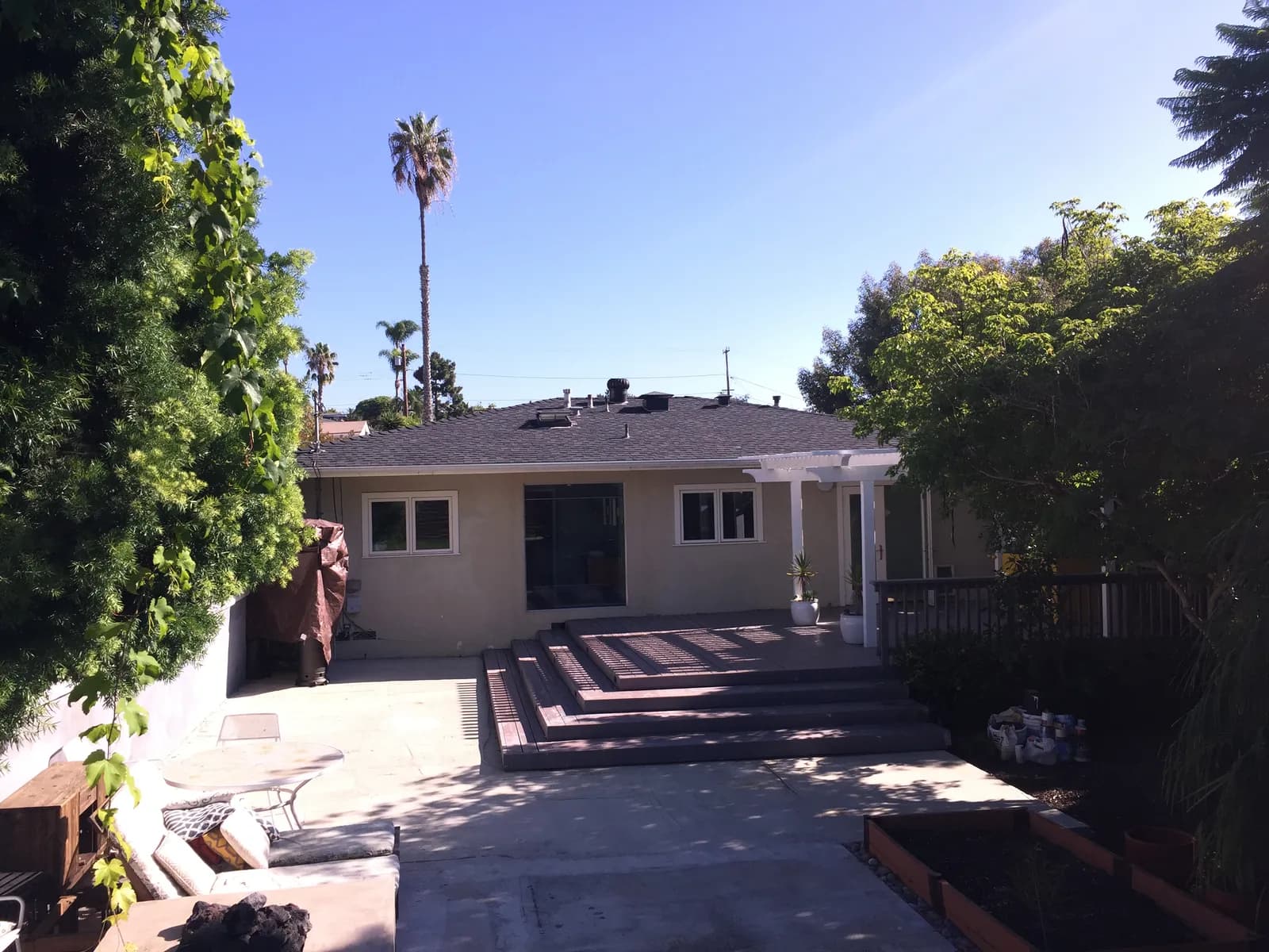 A backyard with a concrete patio, wide deck steps, and a pergola-covered porch at the rear of a house.