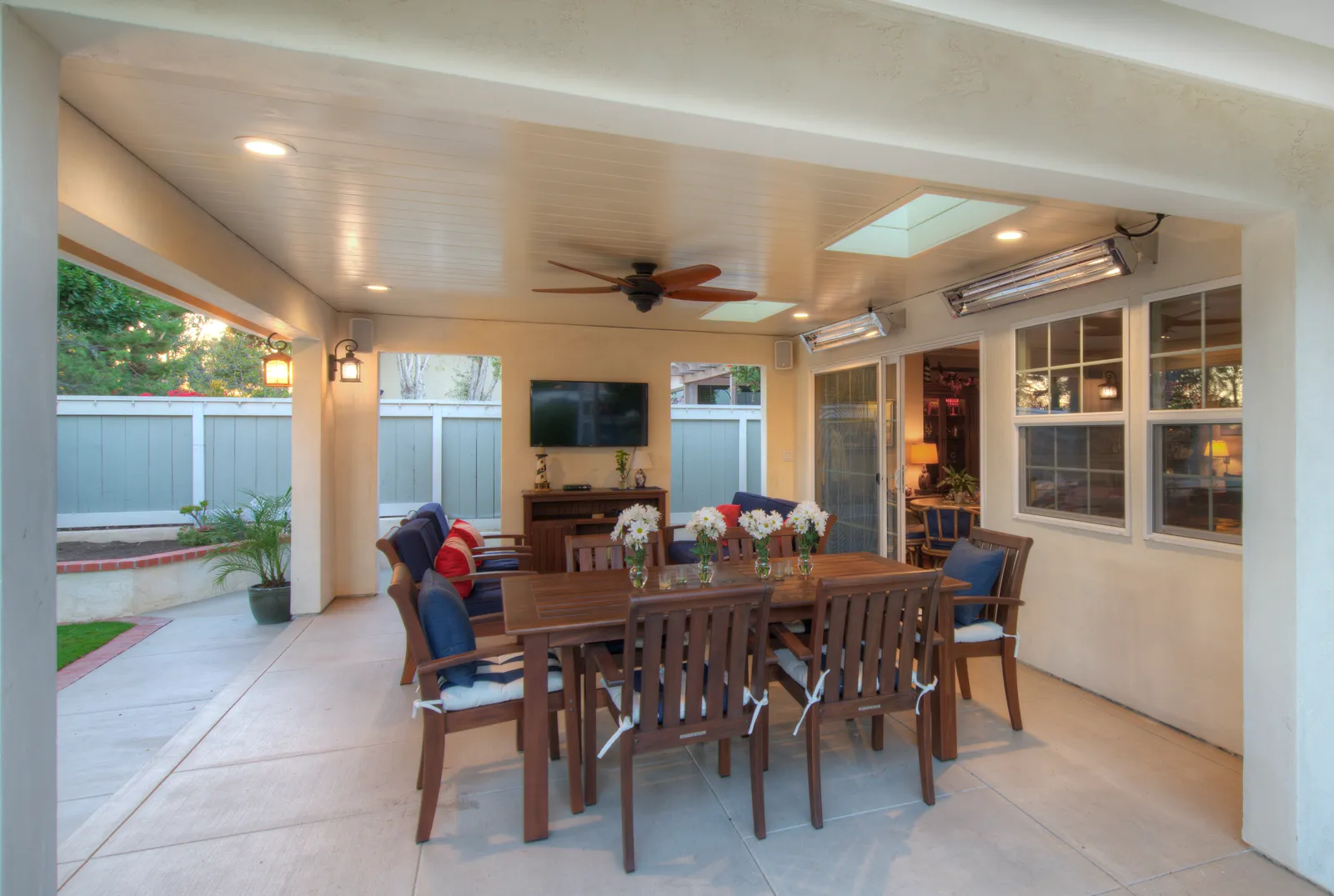 Outdoor patio area with concrete pavers, colorful planted beds, and grass lawn.