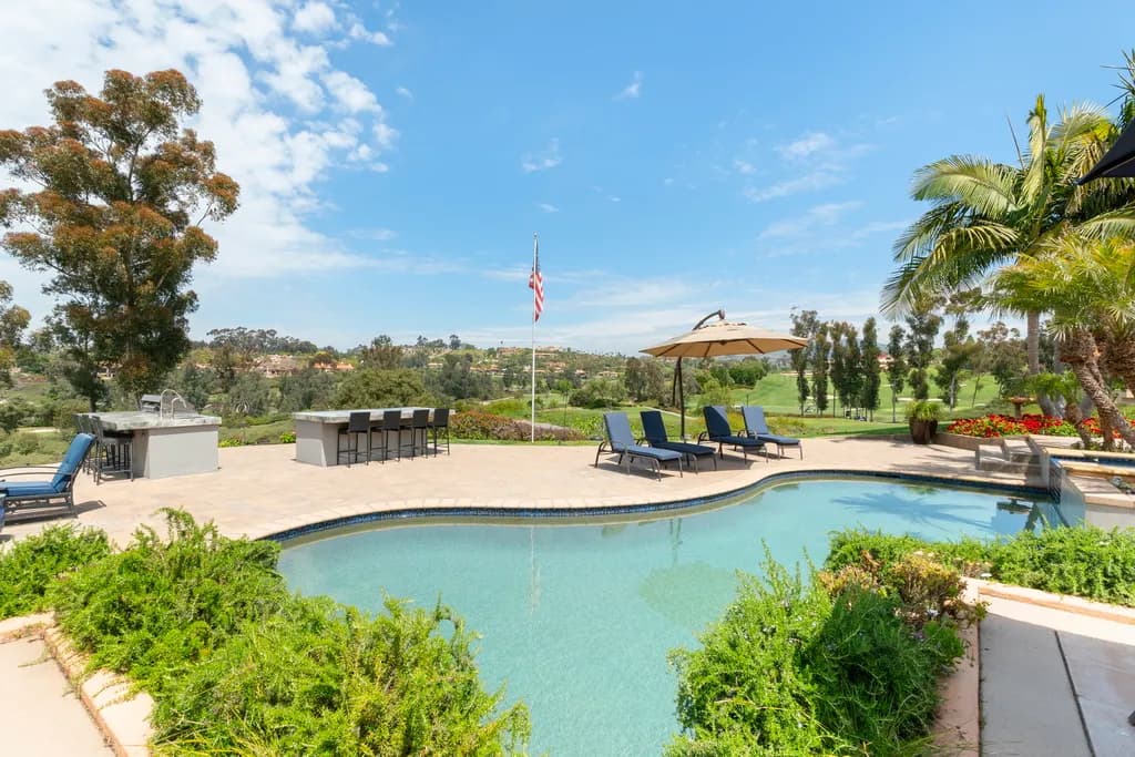 Free-form backyard pool with lounge chairs, cantilever umbrella, and a green fairway view beyond.