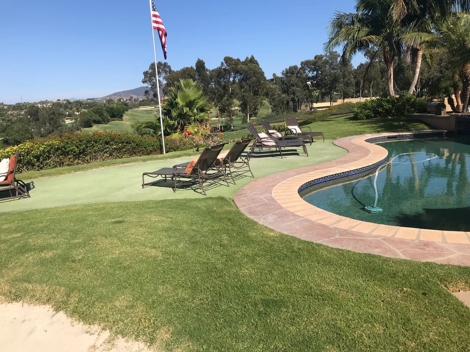 Backyard with curving pool, stamped concrete coping, lounge chairs on a putting green, and a hillside view.