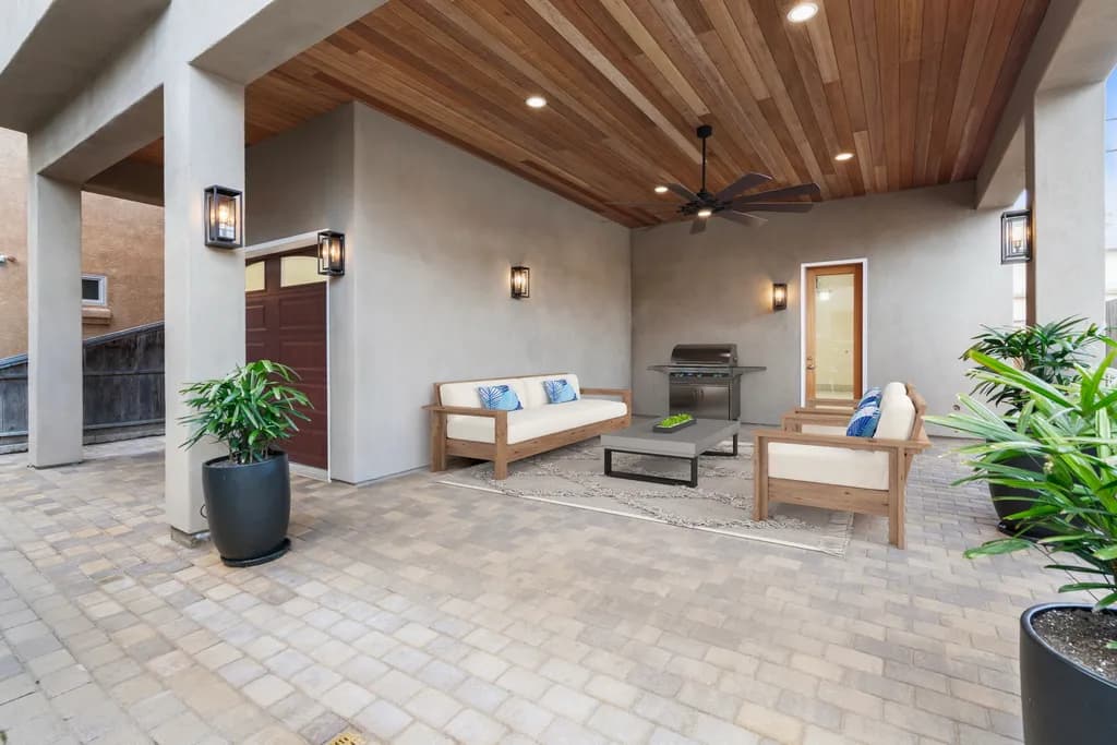 Covered patio with a wood plank ceiling, ceiling fan, outdoor sofas, and paver flooring.