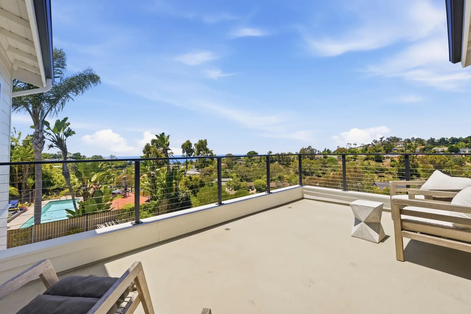 Second-story deck with cable railing, lounge chairs, and a view over treetops to the ocean.