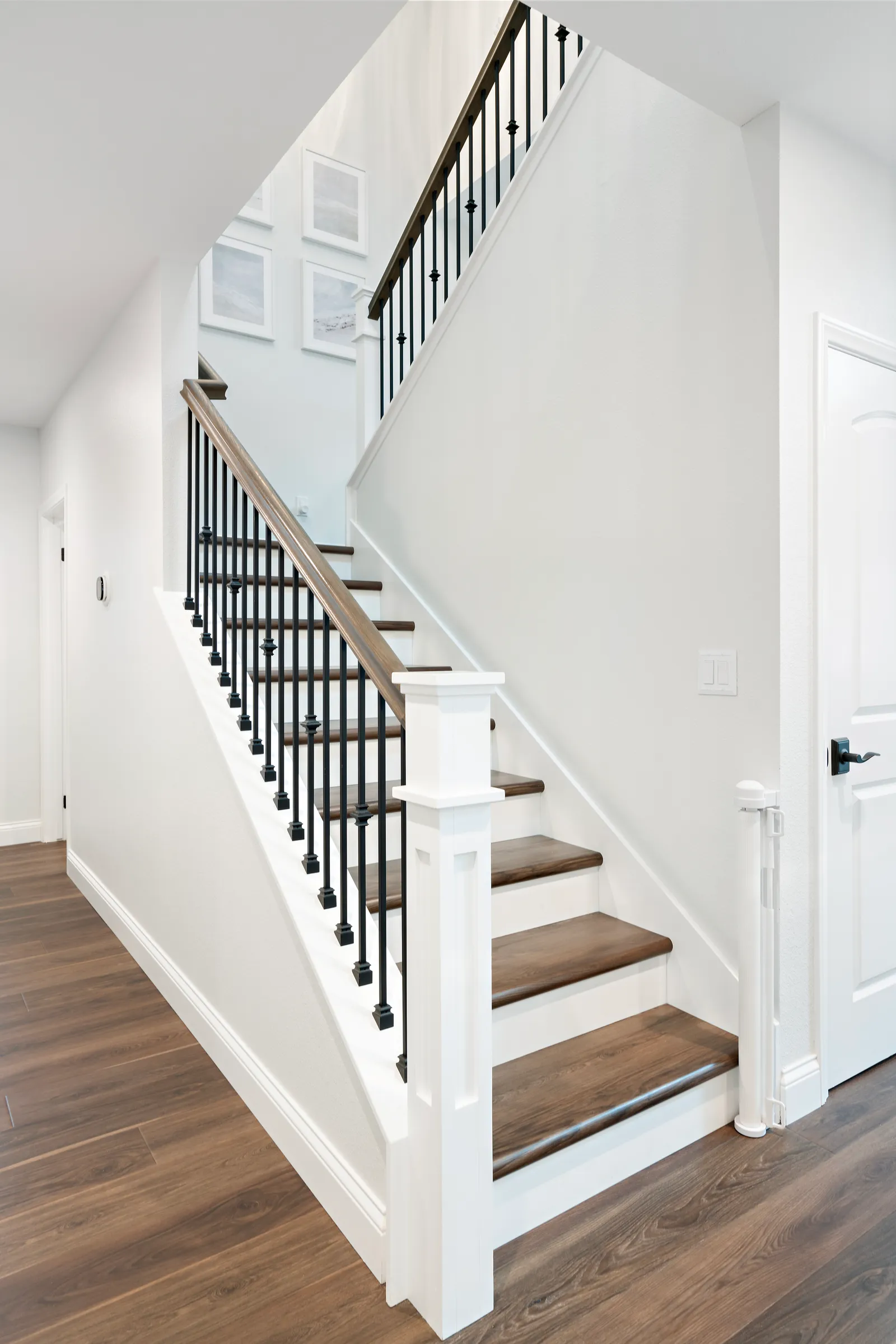 A staircase with wood treads, white risers, iron balusters, and a wood handrail beside dark wood floors.