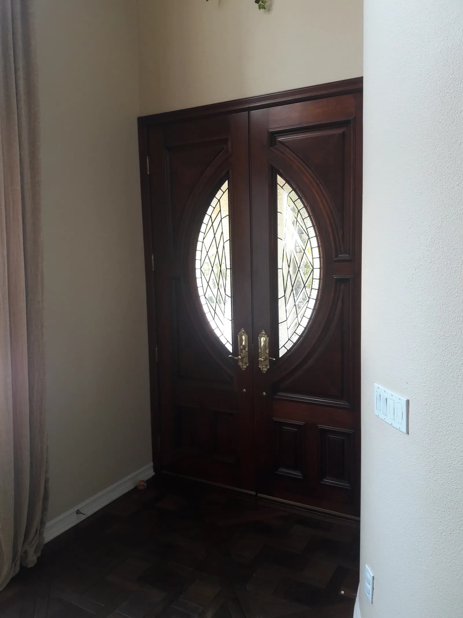 Entry foyer with dark wood double doors featuring oval leaded glass inserts and parquet flooring.