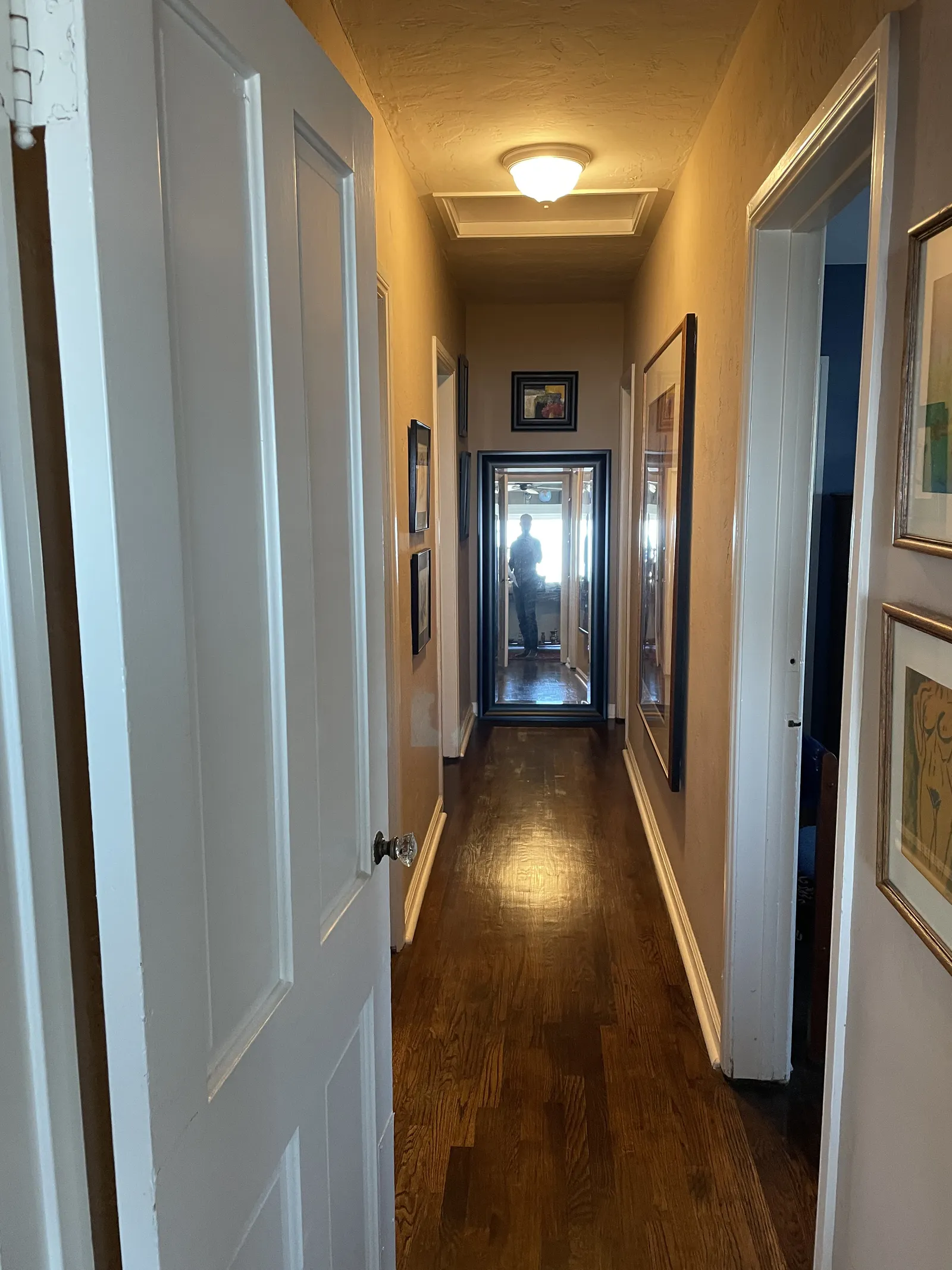 Narrow hallway with refinished hardwood floor, framed artwork, and a tall mirror at the end.