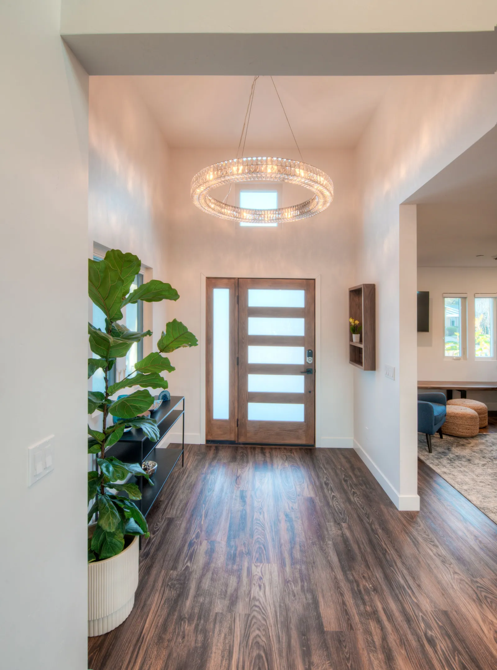 Entry foyer with a crystal ring chandelier, modern wood front door with frosted glass, and dark wood floors.