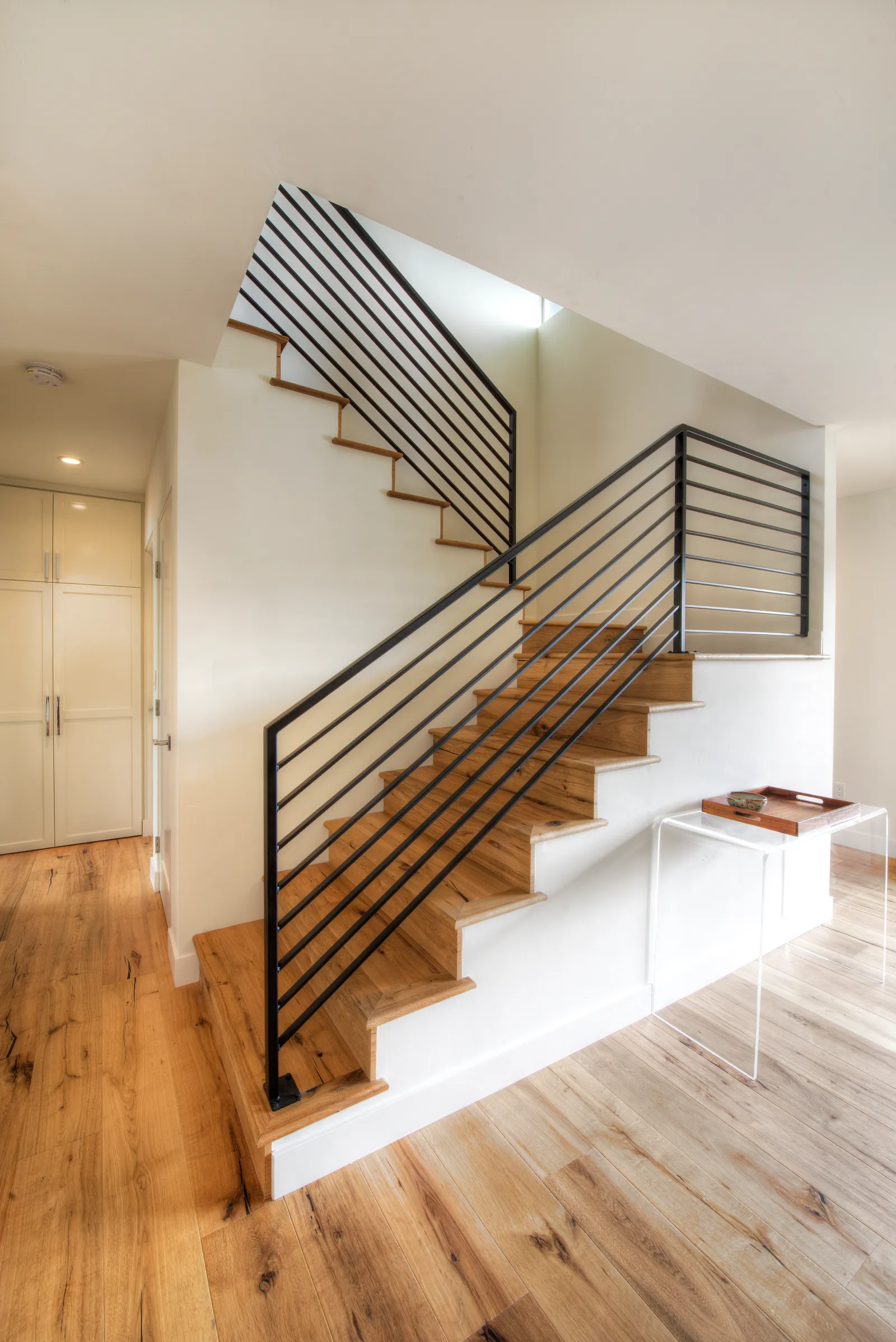 Modern staircase with oak treads, white risers, and black horizontal metal railing beside wide-plank oak flooring.