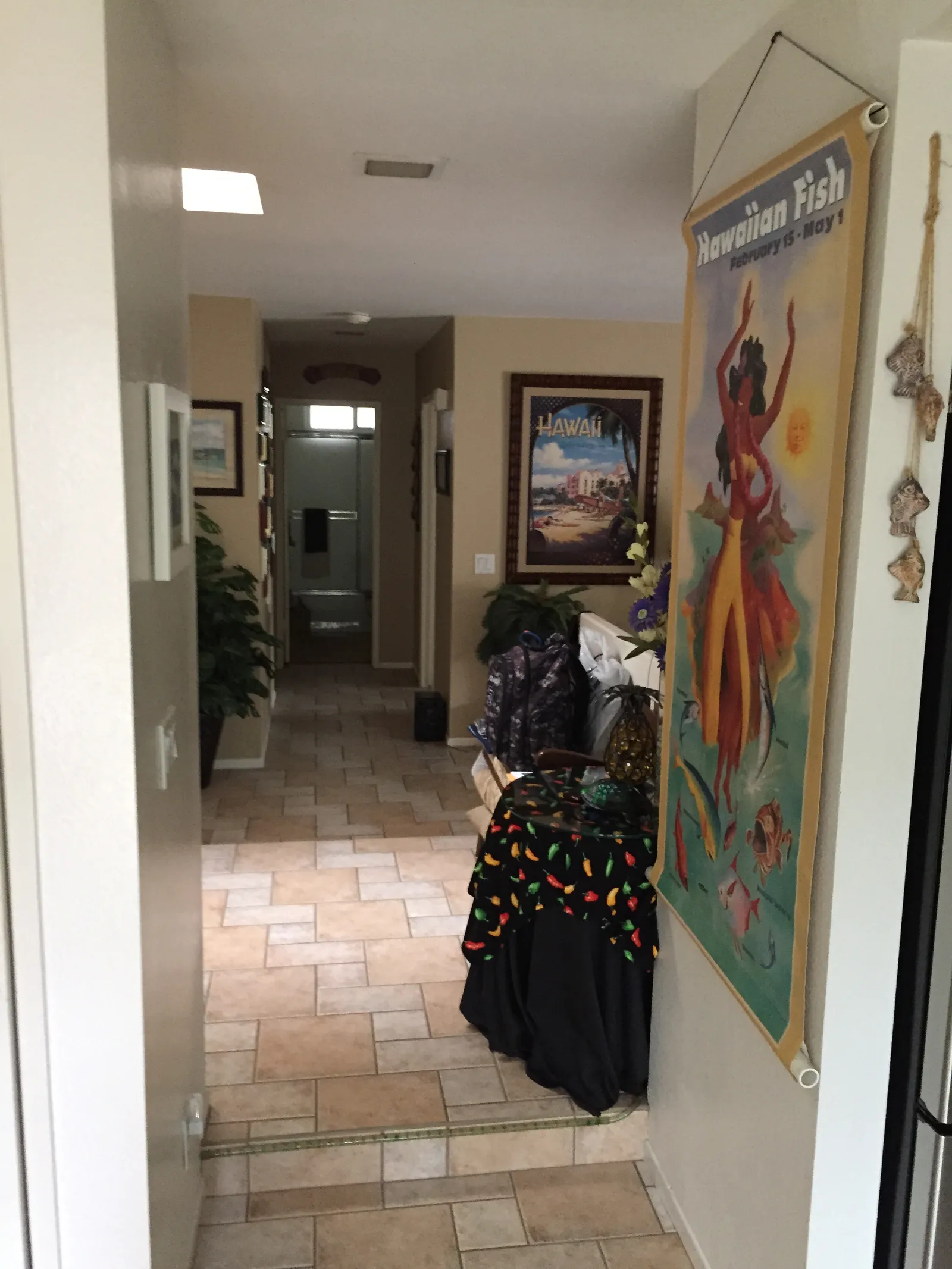 A hallway with beige tile flooring, potted plants and colorful tropical travel posters on the walls.