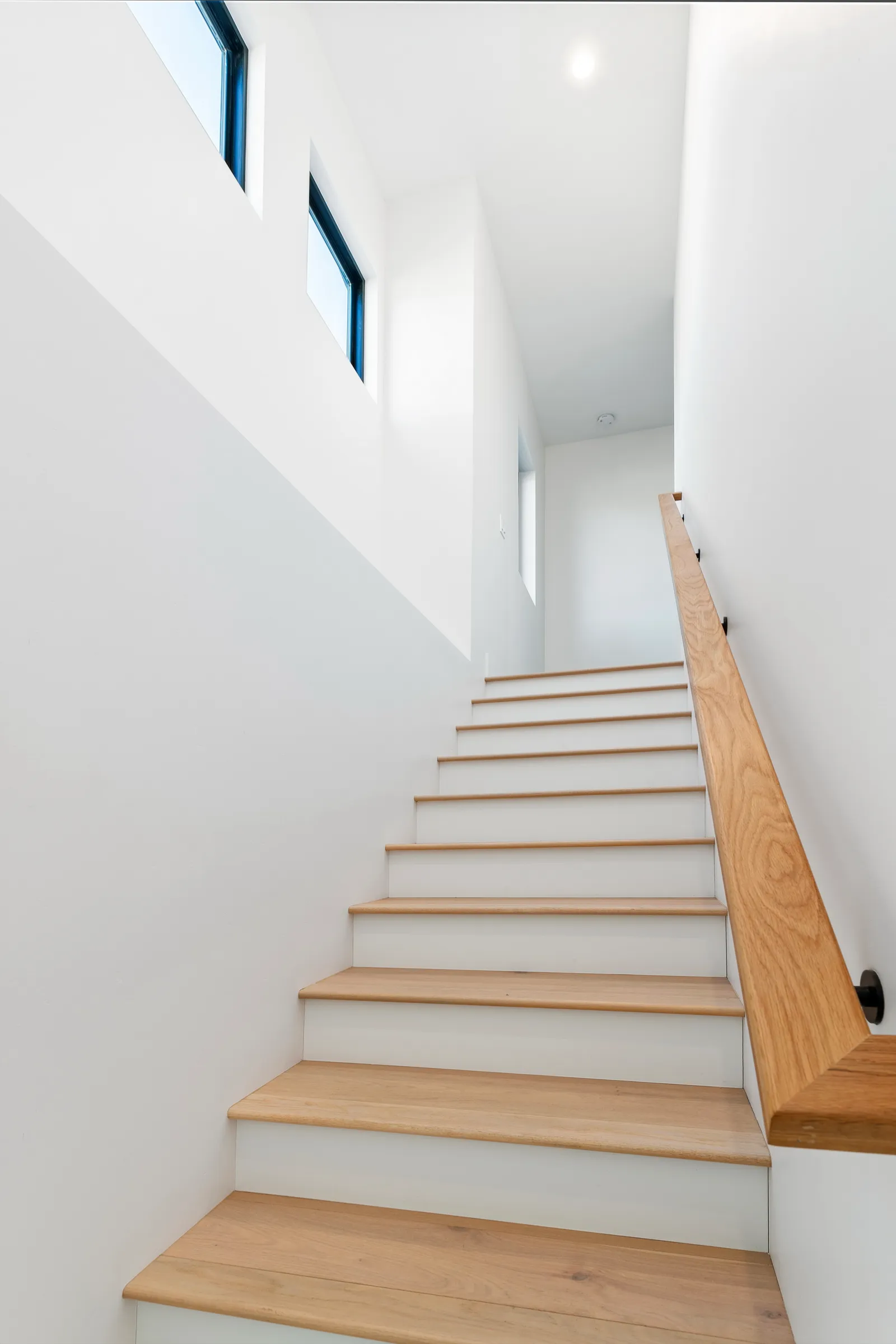 Bright modern staircase with white oak treads and handrail, white risers, and slot windows.