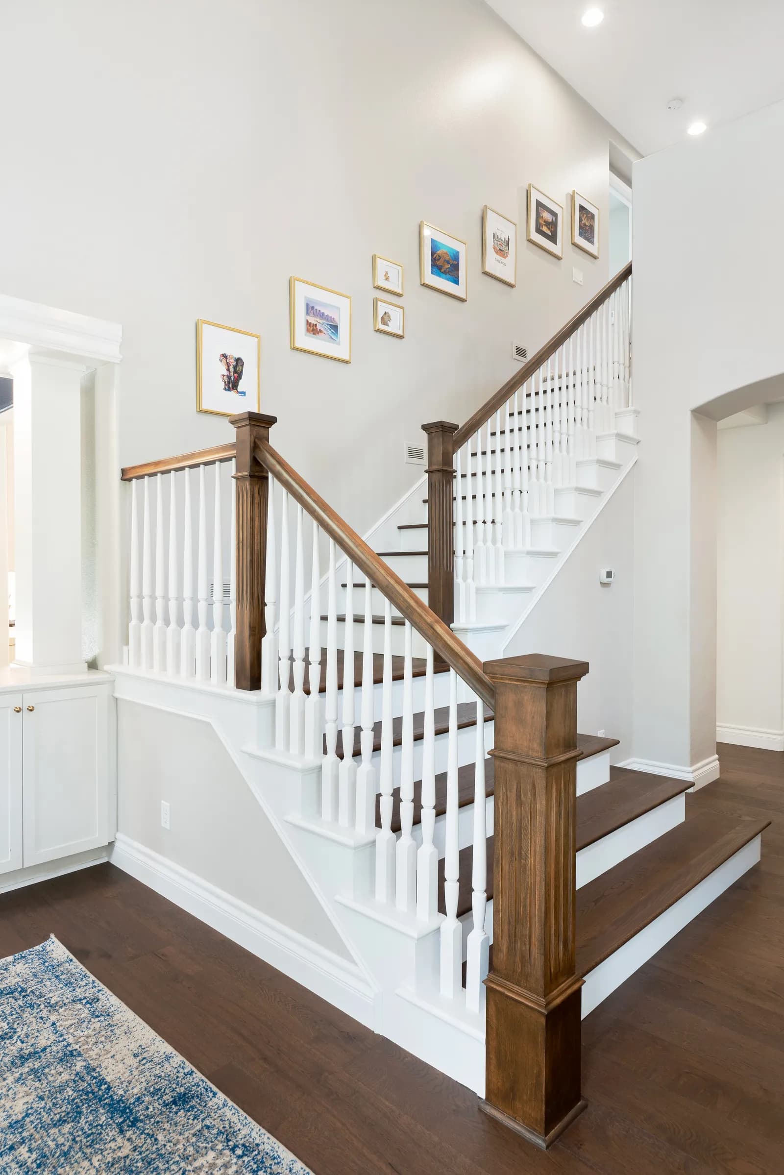 A staircase with white spindles, stained wood handrails and a gallery wall of gold-framed art.