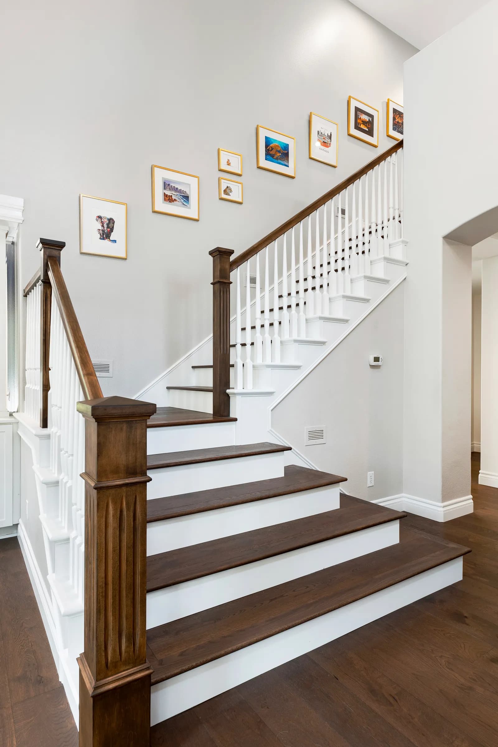 A staircase with dark wood treads, white risers, and spindle railing beneath a wall of framed art.