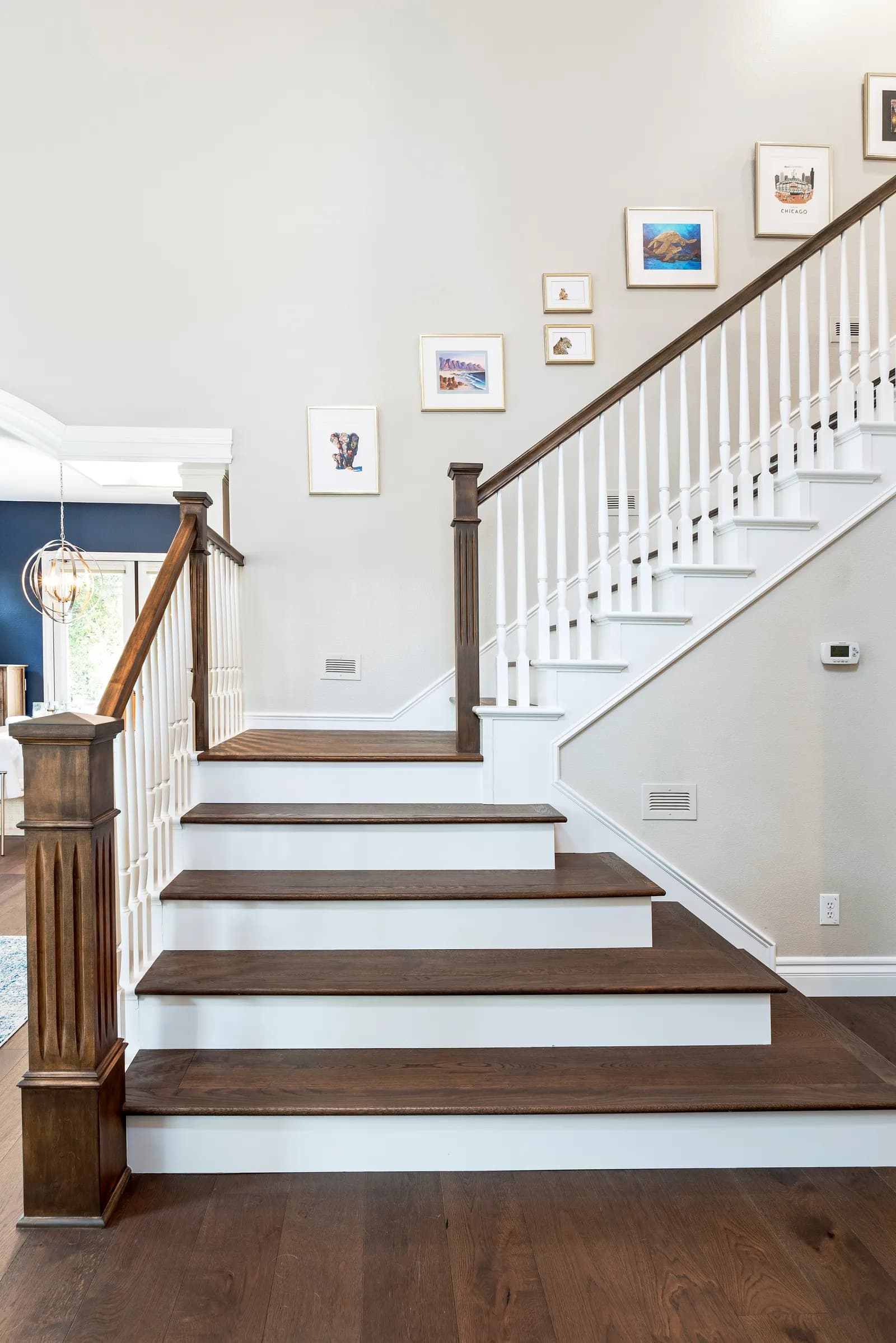 Staircase with dark wood treads, white risers and balusters, wood newel posts, and a gallery wall of framed art.